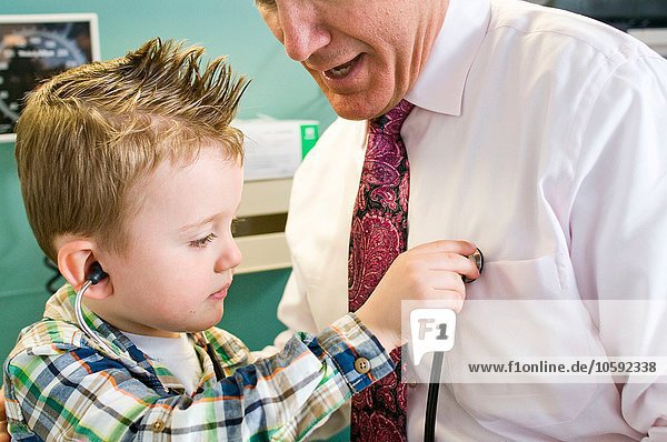 Männlicher Arzt lässt Jungen mit Stethoskop in der Arztpraxis spielen