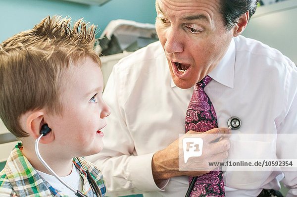 Male doctor letting young boy play with stethoscope in doctor's office