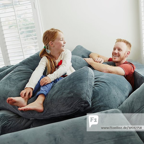 Father and daughter playing on pile of cushions in living room