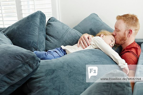 Father and daughter lying on pile of cushions in living room