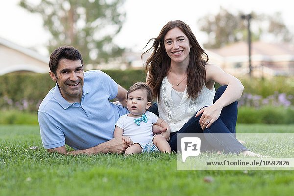 Family with baby boy sitting on grass looking at camera smiling