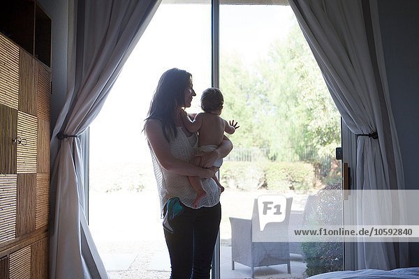 Mother holding baby boy in front of patio door  looking away