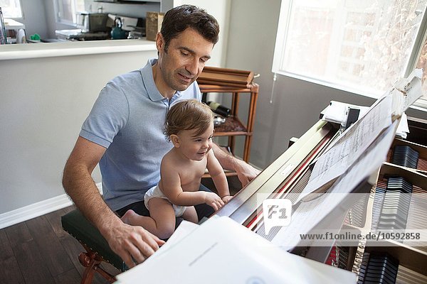 Baby Junge sitzt auf Vaters Knie und spielt Klavier.