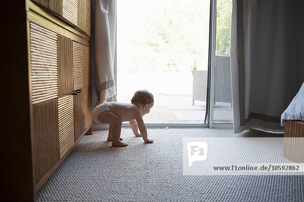 Side view of baby boy on all fours in front of patio doors