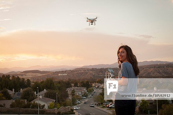 Female commercial operator flying drone above housing development  looking over shoulder at camera  Santa Clarita  California  USA