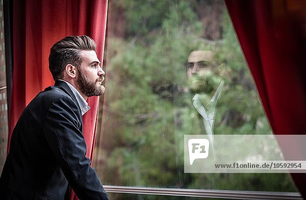 Seitenansicht eines erwachsenen Mannes im Anzug mit Blick aus dem Fenster