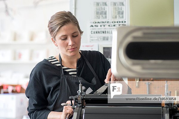 Female letterpress printer inking machine in workshop