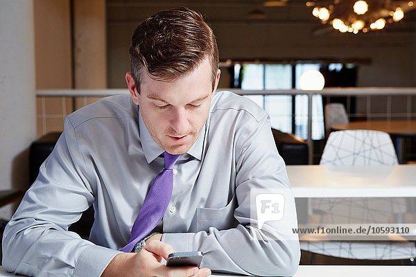 Mid adult businessman sitting at desk  looking at smartphone