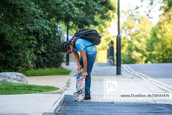 Junge überprüft sein Skateboard auf dem Bürgersteig