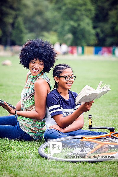 Boy and mother back to back in park reading book