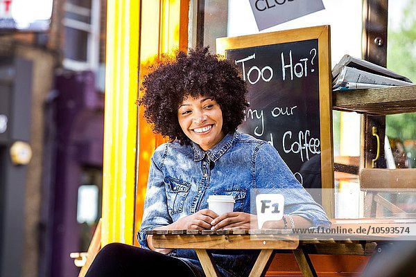 Fröhliche reife Frau trinkt Kaffee zum Mitnehmen und Straßencafé