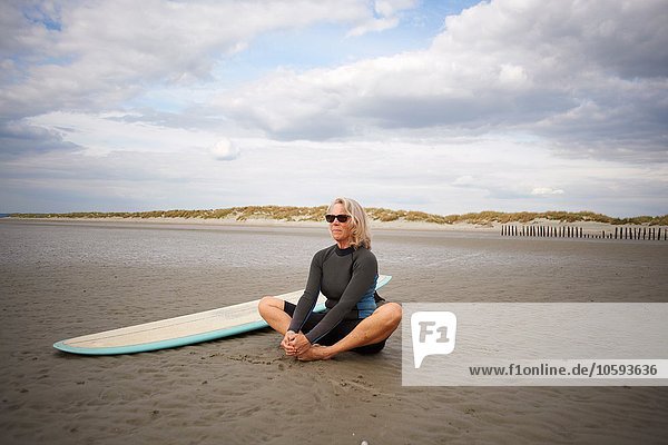 Senior woman relaxing on sand  surfboard beside her