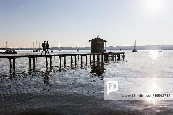 Silhouette des Paares  das auf dem Pier am See zum Bootshaus geht  Schondorf  Ammersee  Bayern  Deutschland