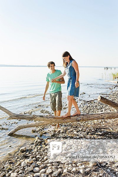 Man helping woman to balance on driftwood  holding hands  Schondorf  Ammersee  Bavaria  Germany