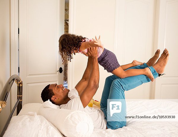 Side view of father lying on bed to lifting up daughter  face to face smiling