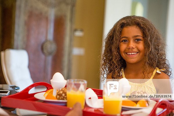 Junges Mädchen mit Frühstückstablett und lächelndem Blick auf die Kamera