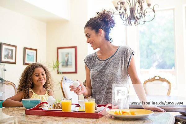 Mother and daughter at home preparing breakfast tray smiling