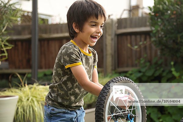 Junge im Garten repariert auf dem Kopf stehendes Fahrrad lächelnd