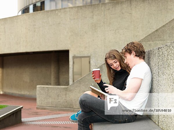 Young couple having coffee  using smartphone on concrete bench  Melbourne  Victoria  Australia