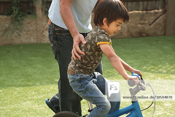 Side view of father supporting boy learning to ride bicycle