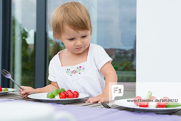 Weibliches Kleinkind beim Blick auf die Mittagsteller auf der Terrasse
