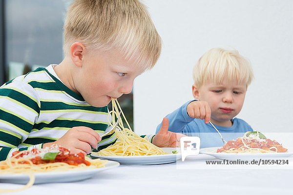 Boy and toddler brother eating spaghetti on patio