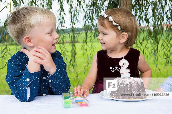 Junge und Kleinkind mit Geburtstagskuchen im Garten