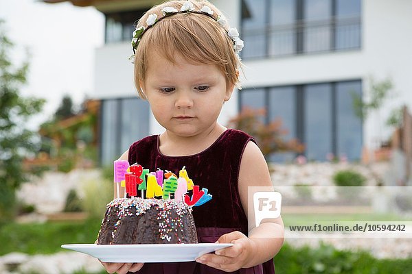 Female toddler carrying birthday cake with candles in garden