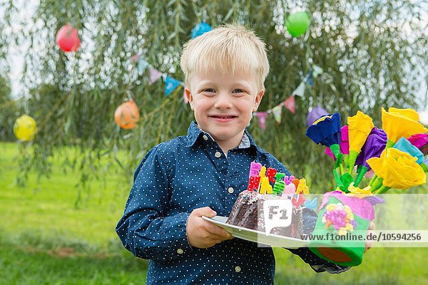 Portrait of boy carrying birthday cake and paper flowers in garden