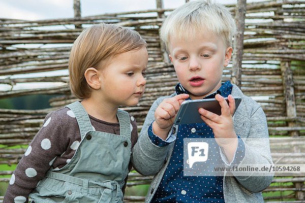 Junge und Kleinkind mit Touchscreen am Smartphone im Garten