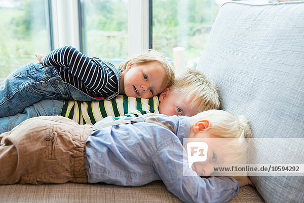 Porträt eines müden Jungen und zweier Kleinkinder  die auf dem Sofa liegen.