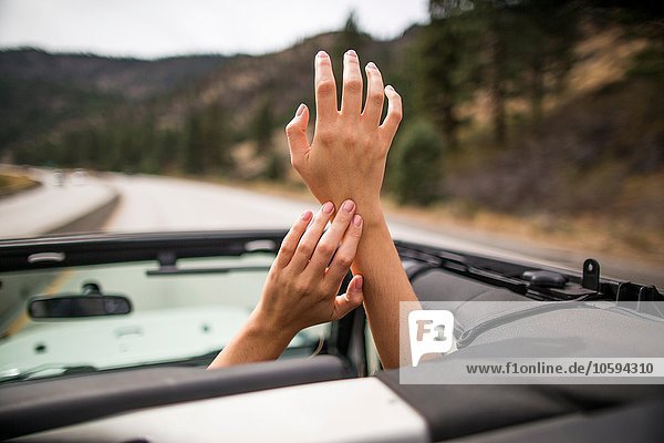 On the road view of young womans hands raised through jeep sunroof