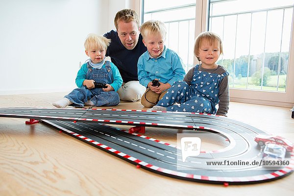 Mid adult man and three young children playing with toy racing cars on living room floor