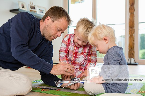 Mid adult man and two sons preparing toy airplane on living room floor