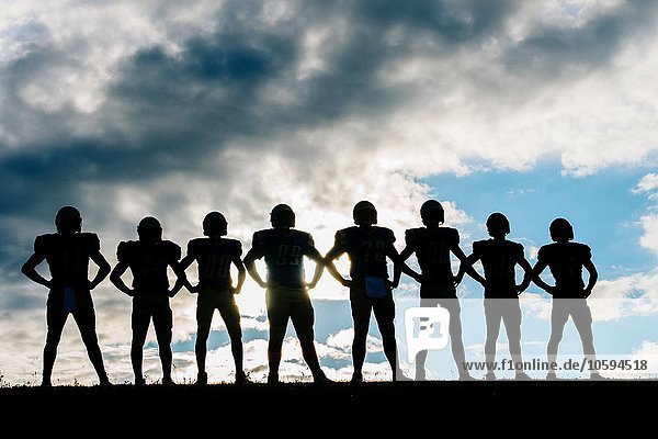Silhouette einer Gruppe junger amerikanischer Fußballspieler  die in einer Reihe stehen  Hände auf den Hüften.