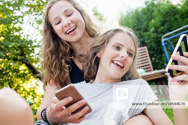 Zwei Teenager-Mädchen beim Lesen von Smartphone-Texten im Garten