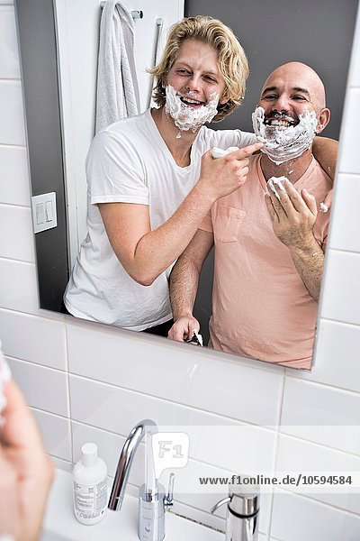 Bathroom mirror image of male couple having fun shaving