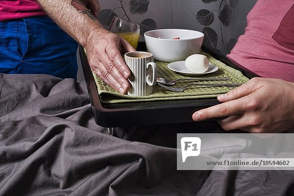Nahaufnahme eines Mannes  der eine Kaffeetasse auf das Frühstückstablett stellt  um seinen Freund im Bett zu sehen.