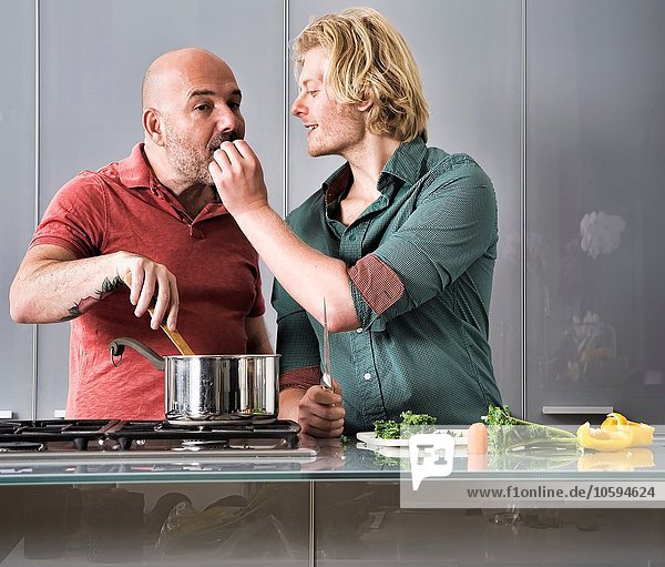 Romantic male couple tasting food whilst cooking in kitchen