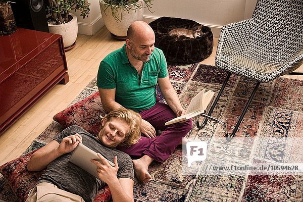 Männliches Paar auf dem Wohnzimmerboden Lesebuch und digitales Tablett
