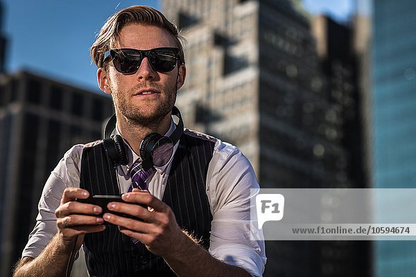 Junger Geschäftsmann vor dem Büro der mit dem Smartphone wegblickt New York USA