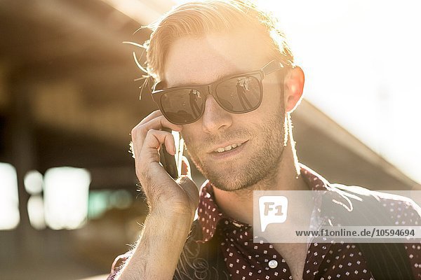 Junger Geschäftsmann mit Sonnenbrille spricht auf dem Smartphone in der Stadt.