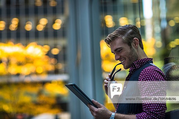 Glücklicher junger Geschäftsmann lehnt sich gegen das Parkfenster und liest digitales Tablett.