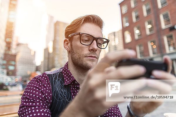 Ernsthafter junger Geschäftsmann liest Smartphone-Text im Bürgersteigcafé  New York  USA