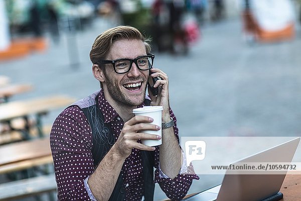 Junger Geschäftsmann beim Plaudern auf dem Smartphone im Bürgersteigcafé
