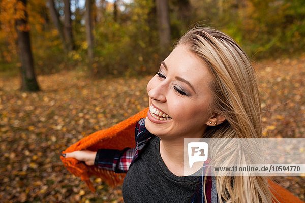 Junge Frau tanzt und hält Decke hoch im Herbstwald