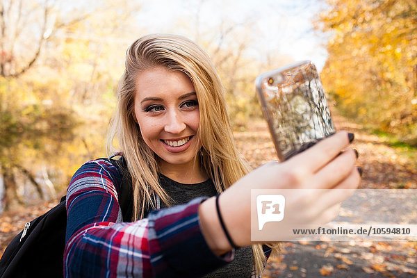 Junge blonde Frau mit Smartphone Selfie im Herbstwald