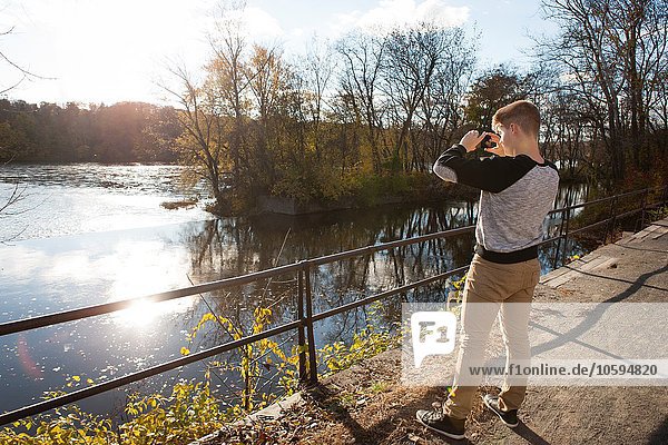 Teenager-Junge fotografiert sonnigen Fluss im Herbstpark