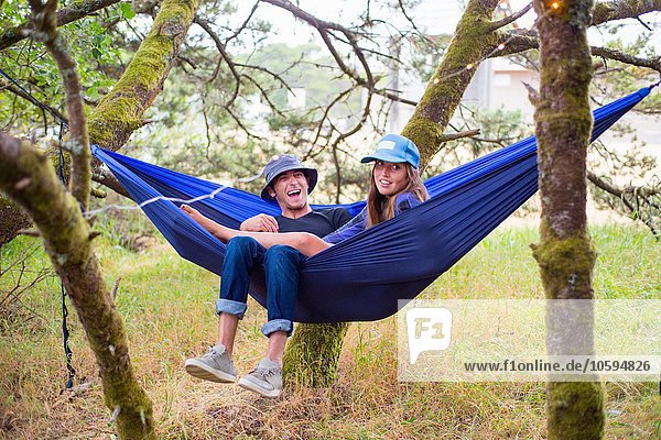 Glückliches erwachsenes Paar in blauer Hängematte zwischen Bäumen liegend