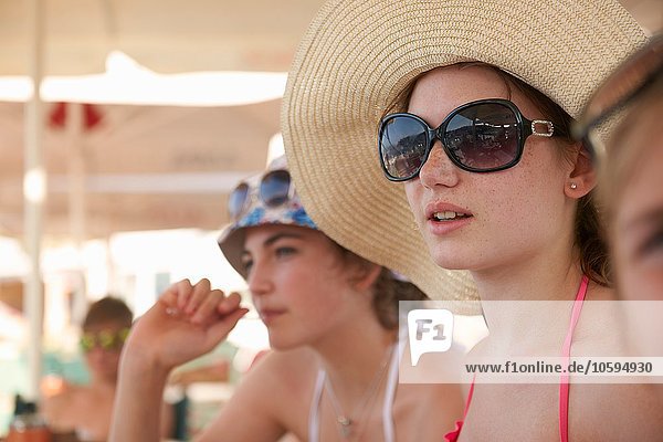 Row of teenage girls wearing sunhats relaxing under beach umbrellas